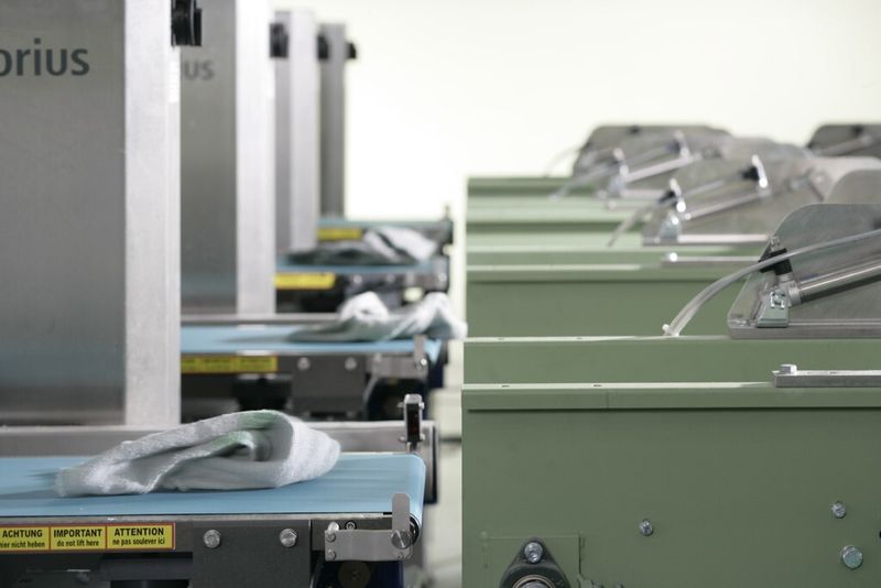 In der computergesteuerten Qualitätsprüfung kontrolliert eine elektronische Waage automatisch das Gewicht jedes einzelnen Tuchs und sortiert die verschlissenen aus. Detektoren untersuchen die Tücher nach eventuell verbliebenen metallischen Rückständen und sortieren diese Tücher ebenso aus. (Bild: Mewa)