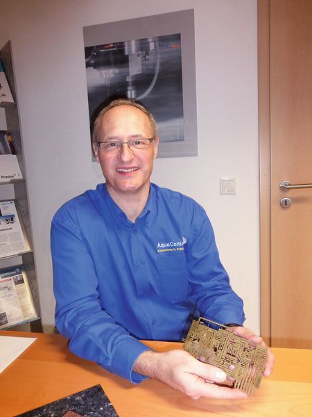 Dipl.-Ing. Harald Lange, Geschäftsführer der Aqua Contour GmbH, zeigt ein elektronisches Bauteil aus Messing. Würde man eine solche Feinstarbeit mit dem Laser oder mit Plasma schneiden, würden die kleinen Spitzen und Stege wegbrennen. Der Wasserstrahl jedoch bringt keine Wärme ins Bauteil ein, deswegen ist er gut geeignet für solch diffizile Aufgaben. (Bild: Finus)