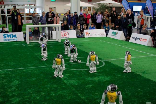 Die Teams bestehen aus je fünf Naos, die auf einem 9 × 6 m² großen Spielfeld gegeneinander antreten und völlig autonom agieren.  (Kickoff / Tim Laue / CC BY-SA 4.0)