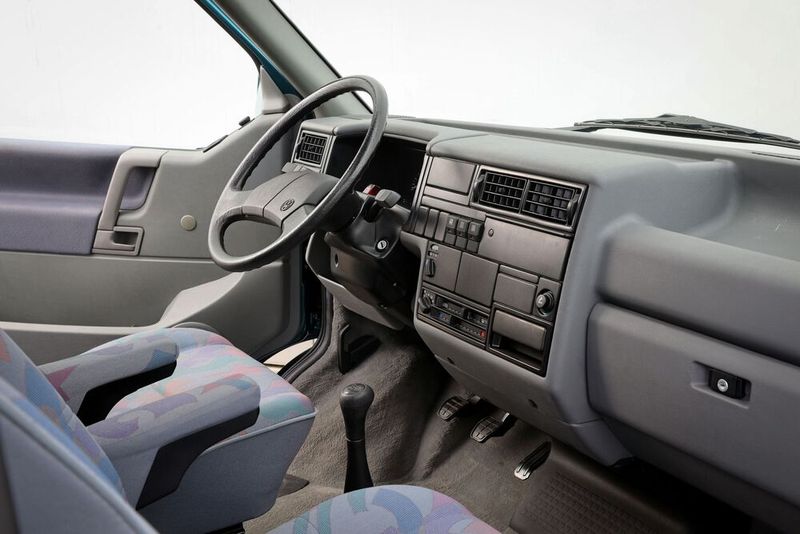 Das Armaturenbrett bzw. Cockpit des T4 war, wie das gesamte Fahrzeug, eine deutlich Verbesserung gegenüber dem Vorgänger. Zum Jahresende 1995 erfuhr der T4 eine „Große Produktaufwertung“ (GP), ein Eigenname von VW für Modellpflege. Bei Multivan, Caravelle und California wurde die Karosserie vorn um acht Zentimeter verlängert. Der bis dahin rechteckige Kühlergrill erhielt bei diesen gehobenen Varianten das damals VW-typische „Happy Face“, zugleich wurden die Scheinwerfer des langen Vorderwagens durch eine keilförmige Verjüngung dynamischer gestaltet und mit weißen statt gelben Blinkleuchten ergänzt. VW wollte damit die Pkw-Versionen äußerlich von den Transporter-Varianten abheben, die das bisherige Gesicht unverändert bis zum Produktionsende beibehielten.  (Bild: Volkswagen Nutzfahrzeuge)