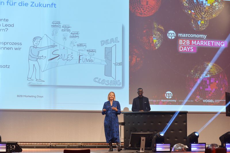 Elena Eberhardt von Schildknecht AG und Ivo Oppong-Addai gaben in ihrem Impulsvortrag Einblicke darin, wie Schildknecht vom traditionellen Mittelständler zum Online-Helden wurde. (marconomy © Johannes Untch)