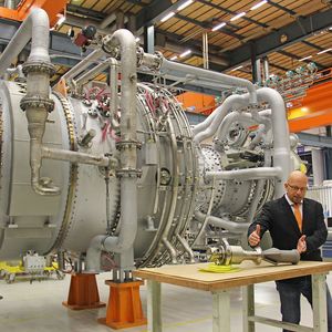 Auf dem Tisch im Vordergrund zeigt Andreas Graichen, Leiter des Teams für additive Fertigung, den Teil des Hauptantriebs, der gedruckt wurde. Im Hintergrund die Gasturbine, in der 28 solcher Antriebe verbaut sind.