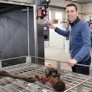 Michael Schmetzer zeigt, wie stark verschmutzte und verölte Eisenbahnteile in einen Frontlader zur Säuberung kommen.