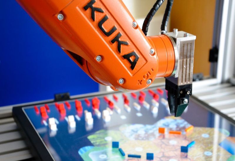 Präzise setzt der Kleinroboter Straßen und Gebäude auf das Bildschirm-Spielbrett von Siedler von Catan. (Kuka Robotics)