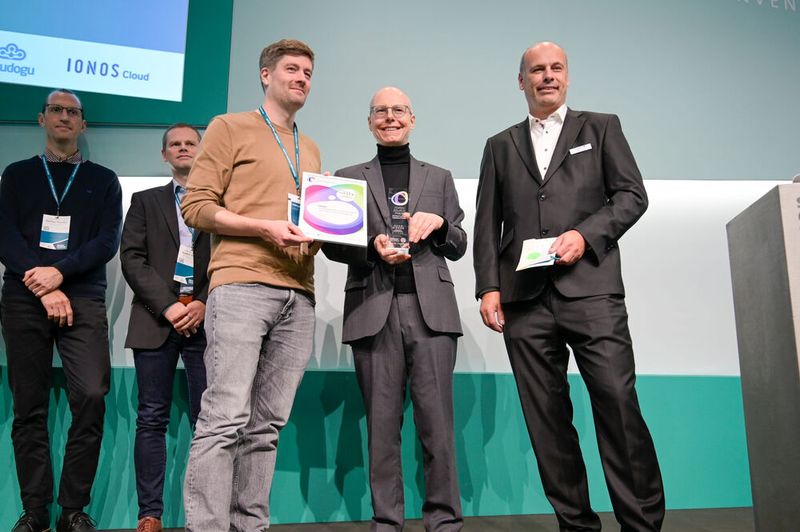 Die Jurymitglieder Stefan Zosel, VP Global Cloud Lead Public Sector bei Capgemini (r.), und Prof. Dr. Dirk Riehle, Professor für Open-Source-Software an der Friedrich-Alexander-Universität Erlangen-Nürnberg (Mitte), überreichen den Preis in der Kategorie „Fachverfahren“ an den Landesbetrieb Geoinformation und Vermessung Hamburg. (Bild: Simon Salzig)