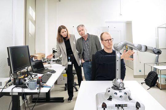 Prof. Dr. Yulia Sandamirskaya et Andreas Leu en arrière plan, tandis que Paul Fox, membre de l'équipe, présente le mouvement interactif du bras robotique avec la caméra 3D (intégrée en bas).(Source : Thomas Entzeroth)