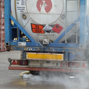 A container with EDA is leaking: From the damaged valve drips the corrosive substance. Fine vapour trails fill the air.