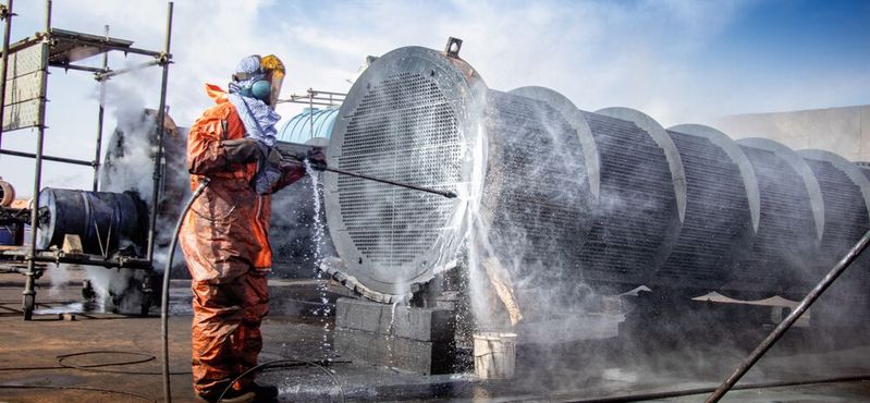 Ein Arbeiter reinigt einen Wärmetauscher: Nicht nur deren Verkalkung an sich kostet viel, sondern auch, dass die gesamte Anlage für Reinigung außer Betrieb gesetzt werden muss. (Bild:  adel - stock.adobe.com)