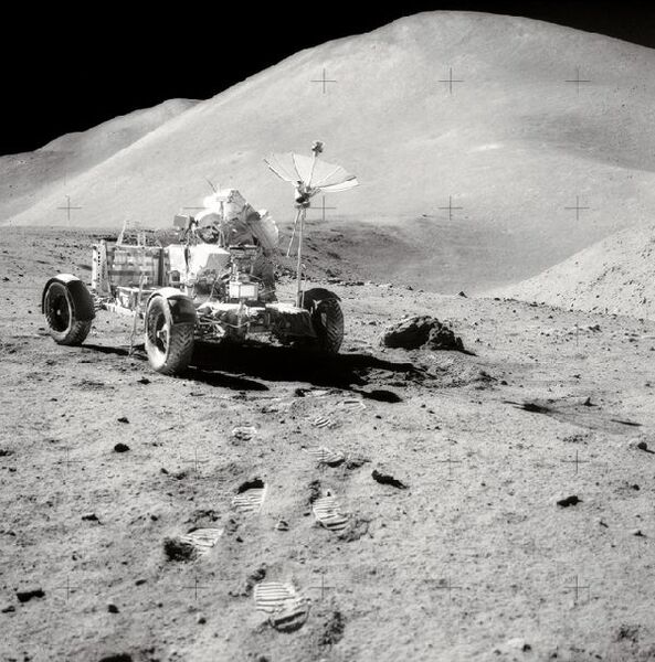 Apollo-15- Kommandant David R. Scott bei der Arbeit am Lunar Roving Vehicle während der EVA 3 am Hadley-Apennine-Landplatz. Rechts in der Bildmitte zu sehen ist Hadley Rille, Hadley Delta im Hintergund ist etwa 4000 m hoch. Oben rechts ist ein Teil des St.-George-Kraters sichtbar. Dieses Foto wurde von James B. Irwin aufgenommen. (Bild: NASA)