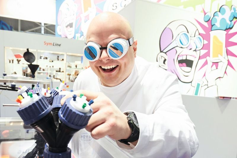 Abb.1: Laborsicherheit geht auch mit Humor: Jan Rittgasser, Marketing-Chef von SCAT, spielt bei einem Messeauftritt vor einigen Jahren den „verrückten Professor“ – das Markenzeichen des Unternehmens. Im Vordergrund ist ein frühes Modell der Safety-Caps zu sehen. Abb.1: Laborsicherheit geht auch mit Humor: Jan Rittgasser, Marketing-Chef von SCAT, spielt bei einem Messeauftritt vor einigen Jahren den „verrückten Professor“ – das Markenzeichen des Unternehmens. Im Vordergrund ist ein frühes Modell der Safety-Caps zu sehen.