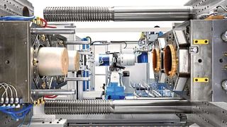 Krauss-Maffei hat mit der GX 1300 eine schlagkräftige Spritzgießmaschine für den Verpackungsbereich entwickelt. Blick in den Arbeitbereich, wo ein Werkzeug für große Kunststoffeimer mit IML-Deko installiert ist. (Krauss-Maffei)