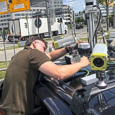 TUM-Forscher Erik Leo Haß prüft die Sensorik auf dem Fahrzeug an einer Kreuzung in Garching-Hochbrück. Aus den unterschiedlichen Echtzeit-Messungen von Kameras, Lidaren und Radaren wird ein permanent aktualisiertes Bild der Verkehrssituation erstellt. (Bild: A.Schmitz / TUM)