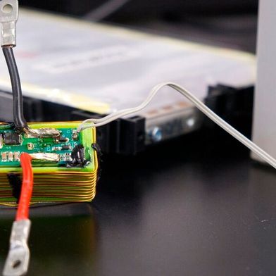 Die grüne Platine enthält den elektronischen Schaltkreis, mit dem die CAU Sensordaten über die vorhandenen Stromanschlüsse einer Batteriezelle übertragen. Die Batteriezelle befindet sich im Hintergrund. (Bild: Christina Anders | Uni Kiel)