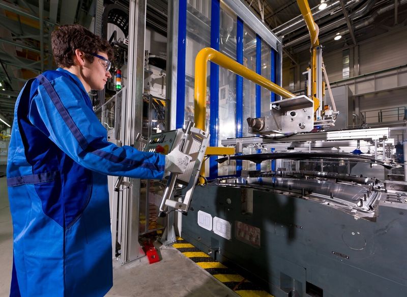 Ein BMW-Mitarbeiter entnimmt mithilfe eines Handlingsystems ein CFK-Karosseriedach aus dem Werkzeug einer RTM-Presse. (Bild: BMW)