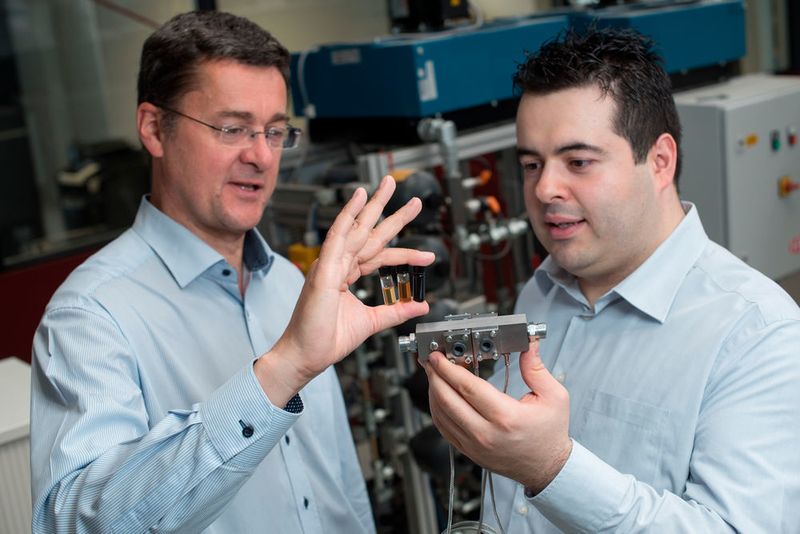 Prof. Andreas Schütze (l.) und Ingenieur Eliseo Pignanelli haben das Messsystem zur Überwachung von Schmieröl mitentwickelt: Auf der Hannover Messe 2017 demonstrieren sie das Analyseverfahren. Wie sichtbar Öl altert, verdeutlichen die Ölproben in den Fläschchen – das linke enthält neues Öl.  (Universität des Saarlandes)