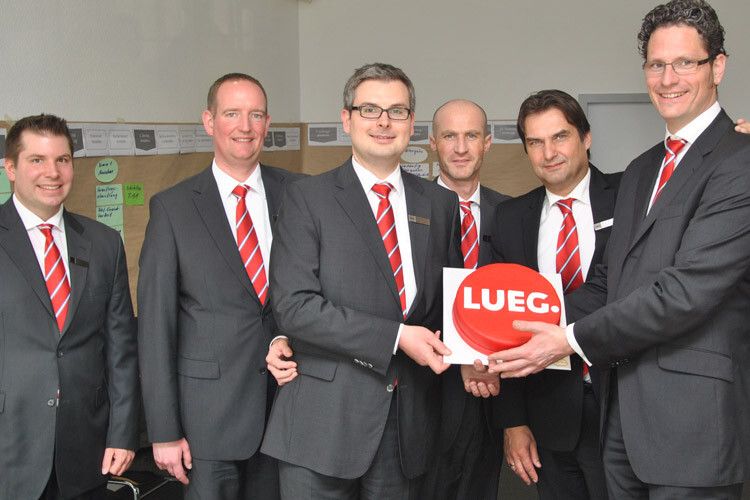 Das Lueg-Team – Christian Schulte-Sasse, Frank Klümper, Benjamin Kaiser, Frank Burbach, Bernd Wrigge und Ralf Schütte – hält einen Kuchen mit der neuen Lueg-CI . (Foto: Michel)