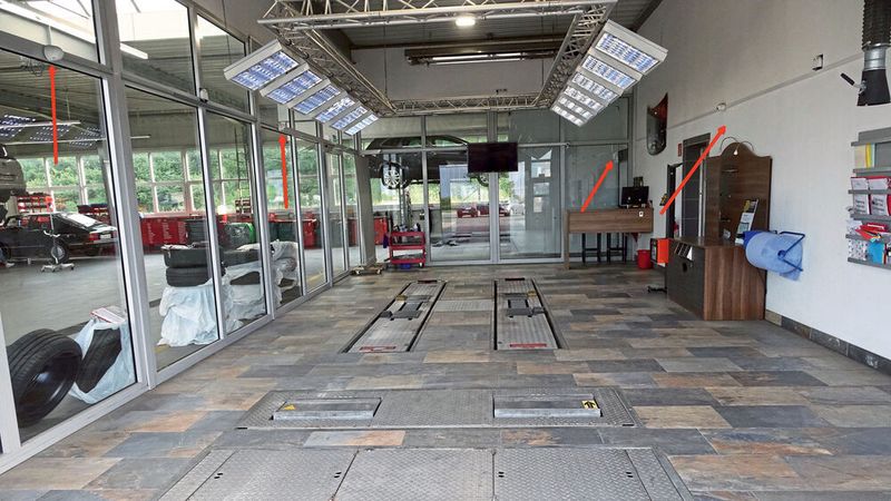 Die Annahmehalle bietet nicht nur jede Menge Licht: An den Wänden sind auch sechs Kameras (Pfeile) angebracht, die von jedem Fahrzeug eine detaillierte Aufnahme machen. Das verhindert Reklamationen des Typs: „Das war vorher aber noch nicht!“ (Bild: Dominsky/»kfz-betrieb«)
