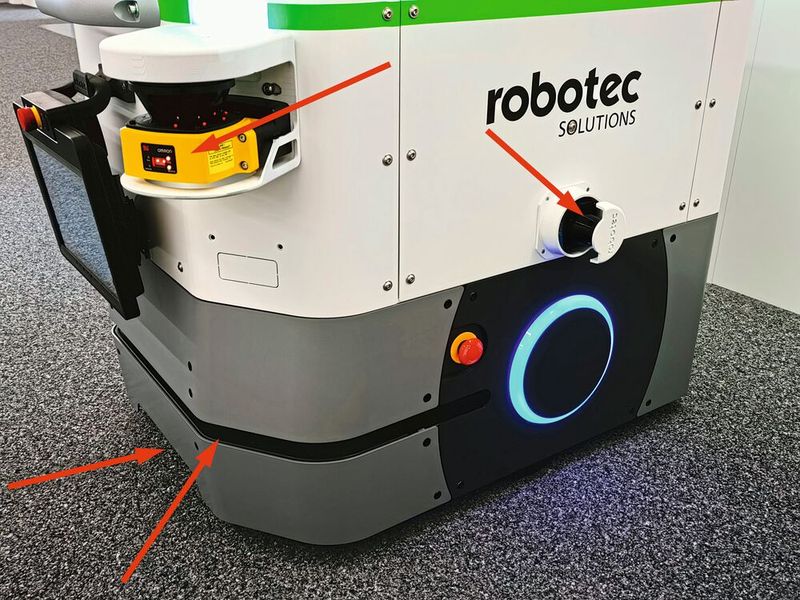 Die autonom navigierende Basis verfügt über zahlreiche Sicherheits-Sensoren: Bodennaher Laserscanner in Fahrtrichtung (Pfeil ganz unten links), darüber ein bodenparalleler 270 ° Laserscanner (Pfeil links), auf jeder Seite ein vertikaler 270 ° Laserscanner (Pfeil rechts) und zwei Weitwinkel-Personendetektoren vorne bzw. hinten (oberer Pfeil). (Bild: Klaus Vollrath)