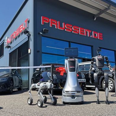 Kollaboratives Trio vor der Autowelt Prusseit in Horb am Neckar: Der rollende Orionstar-Roboter (Mitte) bildet das zentrale Nervensystem, das Quadruped von Unitree (l.) kartografiert das Gelände, der Humanoide (ebenfalls von Unitree) übernimmt Botengänge wie das Holen von Fahrzeugschlüsseln. (Bild: Achter – VCG)