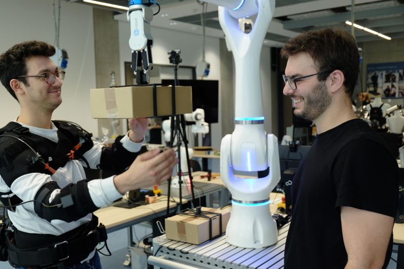 Federico Masiero (li. mit Exoskelett) und Emanuele Aimi testen die Zusammenarbeit mit einem Roboter von Neura Robotics. (Bild: Andreas Schmitz / TUM)