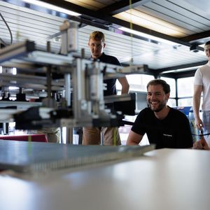 Marco Deffner von Beyond Gravity (z. v. l.) betrachtet einen funktionierenden Prototyp, der eine hochempfindliche Aluminium-Wabenstruktur für Raketenverkleidungen automatisch transportiert.(Bild:  Cyrill Maag)