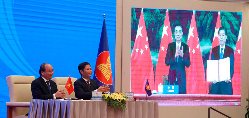 Nguyen Xuan Phuc (l), Premierminister von Vietnam, und Tran Tuan Anh, Handelsminister von Vietnam, applaudieren, während auf einer Leinwand Li Keqiang (l), Ministerpräsident von China, und Zhong Shan, Handelsminister von China, zu sehen sind. Nach achtjährigen Verhandlungen haben China und 14 andere asiatisch-pazifische Staaten das größte Freihandelsabkommen der Welt abgeschlossen.