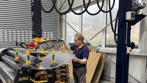 Mit dem Vakuum-Schlauchheber „heavyLIFT“ von Timmer entnimmt ein Mitarbeiter von Lo-Cat Systems das gewölbte Aluminiumblech präzise und schonend aus der Rundwalze. (Bild: Lo-Cat Systems)