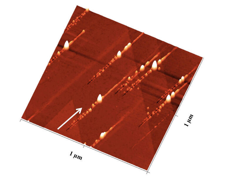 Nanostrukturen nach dem Ionenbeschuss: Der Pfeil zeigt die Richtung der Ionen an: Zunächst ensteht ein Graben mit Nanohillocks an beiden Seiten, ein besonders großer Hügel zeigt den Impakt-Punkt an, danach ist noch eine Erhebung entlang des Pfades zu sehen, den das Ion unter der Oberfläche zurücklegt. (TU Wien)