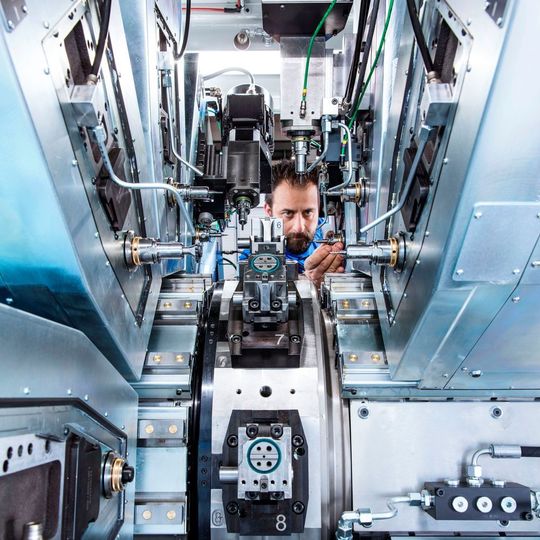 Der doppelt gelagerte vertikale Rundtisch (Bildmitte) dreht sich um eine horizontale Achse. Er taktet die Werkstücke innerhalb von 0,4 s mit einer Positioniergenauigkeit von ± 0,002 mm von Station zu Station. Der doppelt gelagerte vertikale Rundtisch (Bildmitte) dreht sich um eine horizontale Achse. Er taktet die Werkstücke innerhalb von 0,4 s mit einer Positioniergenauigkeit von ± 0,002 mm von Station zu Station.