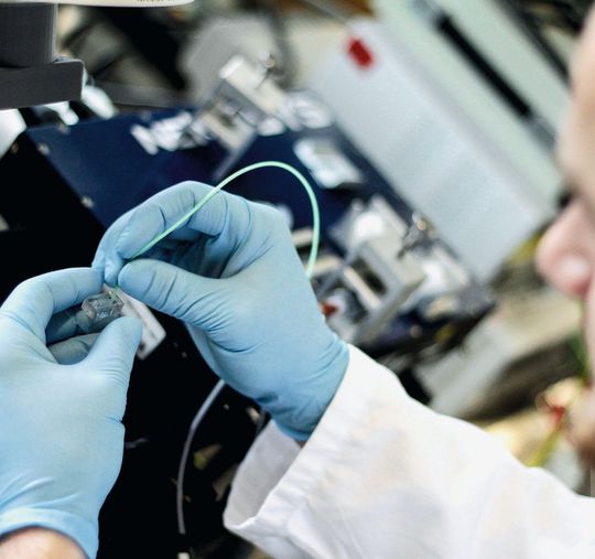 Abb.1: Eine Messung wird vorbereitet: Ein Labormitarbeiter steckt Schläuche in den Chip, über die die suspendierten Zellen in die mikrofluidischen Chips gedrückt werden. Dieser Chip ist eines der wichtigsten Komponenten des Accellerator. Durch diesen mikrofluidischen Chip fließen die Zellen und werden an einem 10 bis 40 Mikrometer breiten Kanal mit bis zu 4000 Bildern pro Sekunde aufgenommen. Abb.1: Eine Messung wird vorbereitet: Ein Labormitarbeiter steckt Schläuche in den Chip, über die die suspendierten Zellen in die mikrofluidischen Chips gedrückt werden. Dieser Chip ist eines der wichtigsten Komponenten des Accellerator. Durch diesen mikrofluidischen Chip fließen die Zellen und werden an einem 10 bis 40 Mikrometer breiten Kanal mit bis zu 4000 Bildern pro Sekunde aufgenommen.