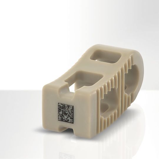 Wirbelsäulenimplantat aus PEEK mit lasermarkiertem UDI-Datamatrix-Code von zirka 3 x 3 mm Größe. Wirbelsäulenimplantat aus PEEK mit lasermarkiertem UDI-Datamatrix-Code von zirka 3 x 3 mm Größe.