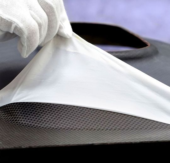 Händischer Abzugsvorgang einer Flexplas-Trenn- und Schutzfolie, entwickelt vom Fraunhofer-Institut für Fertigungstechnik und Angewandte Materialforschung (IFAM), von einem kontaminationsfreien CFK-Bauteil nach dessen Aushärtung in der Heizpresse. Händischer Abzugsvorgang einer Flexplas-Trenn- und Schutzfolie, entwickelt vom Fraunhofer-Institut für Fertigungstechnik und Angewandte Materialforschung (IFAM), von einem kontaminationsfreien CFK-Bauteil nach dessen Aushärtung in der Heizpresse.