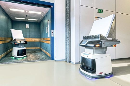 Ein FTS wartet, bis das andere den Aufzug verlassen hat. Dann geht es weiter zu den Maschinen.