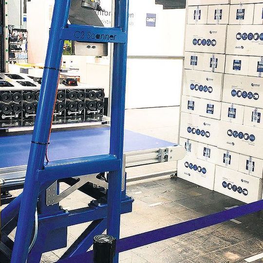 Über dem blauen Förderband zur weiteren Abfuhr der Pakete nach links ist der Vakuumgreifer mit den Scanner-Modulen zu erkennen. Über dem blauen Förderband zur weiteren Abfuhr der Pakete nach links ist der Vakuumgreifer mit den Scanner-Modulen zu erkennen.