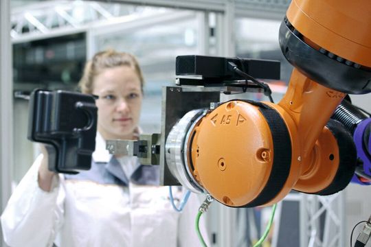 Mit einer neuen Technologie erkennt ein Schwerlastroboter die Bauteile, die eine Mitarbeiterin hält und folgt behutsam ihrer Hand bis zur Übergabe des Werkstücks. Mit einer neuen Technologie erkennt ein Schwerlastroboter die Bauteile, die eine Mitarbeiterin hält und folgt behutsam ihrer Hand bis zur Übergabe des Werkstücks.