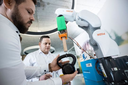 Der Polygreifer (v.l.): Fabian v. Northeim (Eta Opt) und Sascha Mechthold (Uni Kassel) mit einem Prototypen des Polygreifers. Die Platine mit dem Polymer befindet sich in der Vertiefung des Plastikaufsatzes und hält das Holzstück mit dem Gewicht.