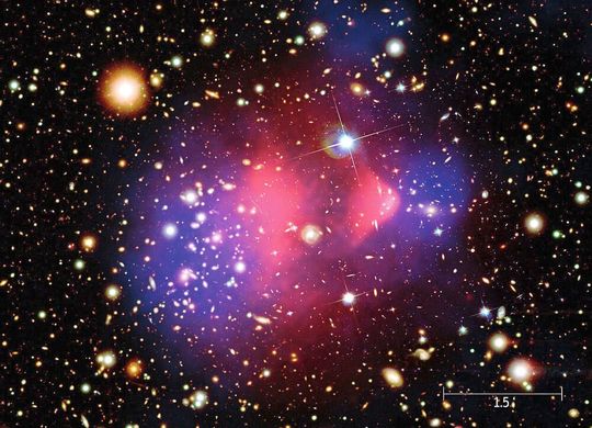 Blick auf Dunkle Materie: Dieses Foto – eine Montage aus mehreren Bildern – zeigt die kollidierenden Galaxienhaufen 1E 0657-56, besser bekannt unter dem Namen „Bullet Cluster“. Den im Hintergrundbild sichtbaren Galaxien im optischen Licht überlagert sind die Röntgenstrahlung der intergalaktischen Gaswolken (pink) sowie die aus Gravitationslinseneffekten berechnete Masseverteilung und damit indirekt die Dunkle Materie (blau). Blick auf Dunkle Materie: Dieses Foto – eine Montage aus mehreren Bildern – zeigt die kollidierenden Galaxienhaufen 1E 0657-56, besser bekannt unter dem Namen „Bullet Cluster“. Den im Hintergrundbild sichtbaren Galaxien im optischen Licht überlagert sind die Röntgenstrahlung der intergalaktischen Gaswolken (pink) sowie die aus Gravitationslinseneffekten berechnete Masseverteilung und damit indirekt die Dunkle Materie (blau).