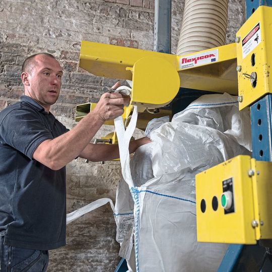 Operator attaches bag loops to the four retractable bag hooks on the fill head. Operator attaches bag loops to the four retractable bag hooks on the fill head.