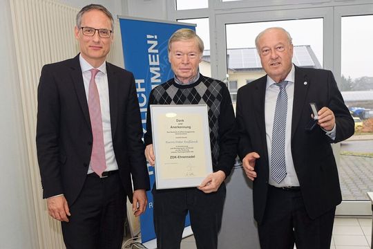 Geehrt: Geschäftsführer Jens Bleutge (li.) und Präsident Hans-Werner Norren (re.) überreichen Peter Reißmann, Ehrenobermeister der Kfz-Innung Westpfalz, die ZDK-Ehrennadel.