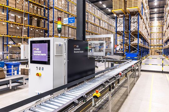 Der Automated Document Inserter platziert Dokumente automatisch auf den Paketen auf dem Fließband. Der Automated Document Inserter platziert Dokumente automatisch auf den Paketen auf dem Fließband.