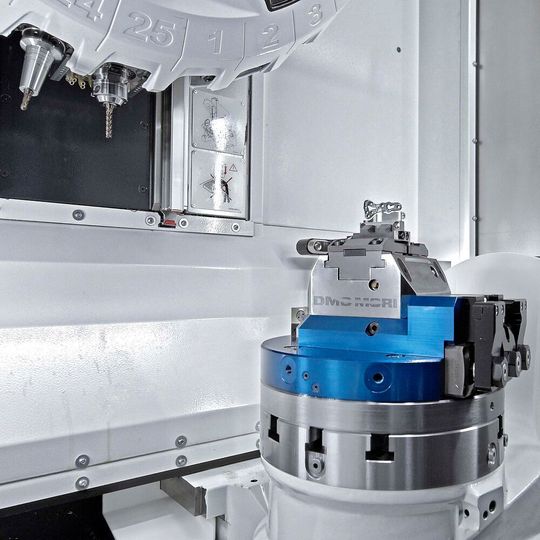 The working area of a DMP 35 fitted with the options of a 25-position tool magazine and an integrated swivelling rotary table for 5-axis machining. The working area of a DMP 35 fitted with the options of a 25-position tool magazine and an integrated swivelling rotary table for 5-axis machining.