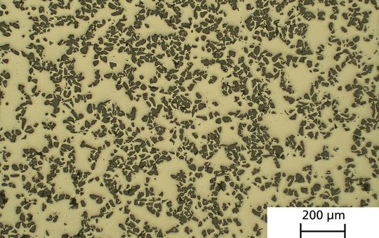 Die hellen Flächen auf dem Schliffbild bestehen aus einer Aluminium-Titan-Mangan-Matrix, bei den dunklen Punkten handelt es sich um keramische Hartpartikel. Während konventionelle Aluminium-Legierungen bei 560° C schmelzen, bleibt dieses Material bis über 1000° c stabil.