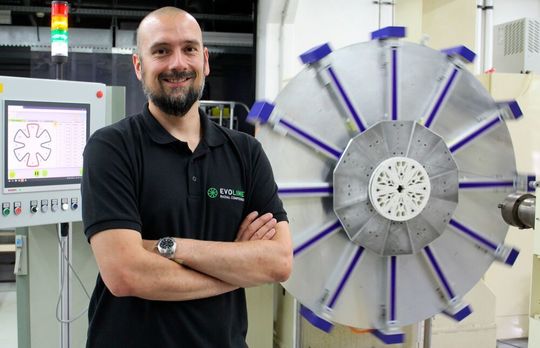 Verbundwerkstoffspezialist Dr. Marcel Bücker vor der laufenden Produktionsanlage, mit deren Hilfe die Fertigung von Speichenrädern aus Verbundwerkstoffen optimiert werden kann. Hier befindet man sich im letzten Schritt, bei dem der Außenring gewickelt wird. Verbundwerkstoffspezialist Dr. Marcel Bücker vor der laufenden Produktionsanlage, mit deren Hilfe die Fertigung von Speichenrädern aus Verbundwerkstoffen optimiert werden kann. Hier befindet man sich im letzten Schritt, bei dem der Außenring gewickelt wird.