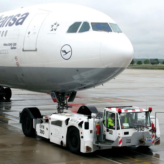 Das Bugfahrwerk auf der Transportplattform eines stangenlosen Spezialschleppers mechanisch verriegelt, wird ein Airbus A 340-300 wie ein Ein-Achs-Anhänger über das Vorfeld des Münchener Flughafens gezogen. Bild: EFM Das Bugfahrwerk auf der Transportplattform eines stangenlosen Spezialschleppers mechanisch verriegelt, wird ein Airbus A 340-300 wie ein Ein-Achs-Anhänger über das Vorfeld des Münchener Flughafens gezogen. Bild: EFM