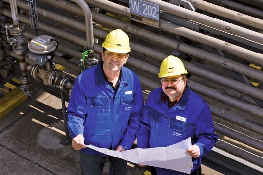 Den Plan für die Umbauten in der Hand: A. Kaceri (links) und W. Meyer vor einem Wasserkühler in der Hydraminfabrik in G 500. (Bild: H.-J. Doelger, BASF)
