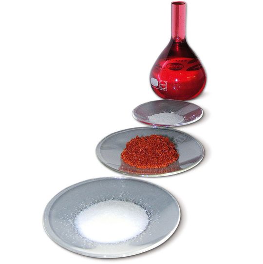 Das Bild zeigt von vorn nach hinten den Scavenger vor der Beladung mit Edelmetall, die rot-orange Probe des mit Rhodium beladenen Scavengers, die Reste des edelmetallfreien Scavengers, nachdem das Edelmetall im Recyclingprozess wieder abgelöst wurde sowie die rhodiumhaltige Lösung, aus der sich das Metall wieder gewinnen lässt. (Bild: Heraeus)