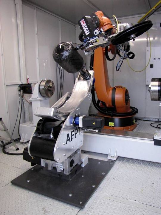 Automatische Fertigung von Druckbehältern: Das Anlagenkonzept basiert auf einem Sechs-Achs-Knickarmroboter, einem kompakten Tapelegekopf und einem sogenannten Tumble-Winder, der den zu bewickelnden Grundkörper (Liner) aufnimmt. Das Zusammenwirken von Roboter und Tumble-Winder führt zur Optimierung der Bahnbewegungen. (Bild: AFPT)