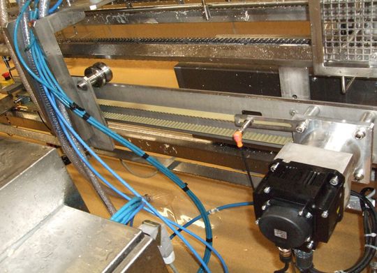 Der Servomotor treibt über einen Zahnriemen den Verfahrwagen an. Ein induktiver Sensor registriert den Abstand der Nocken auf dem Laufband, worüber die SPS die Geschwindigkeit des Verfahrwagens errechnet.