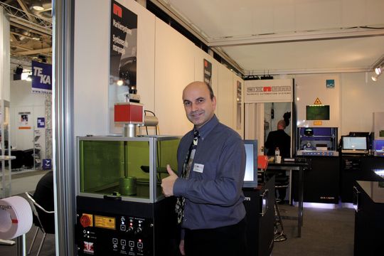 Mike Machule (Verkauf/Productmanager AxNum AG) am Prodexstand neben einem Lasermarkiersystem i103L-G. Der Laser des Systems hat eine Wellenlänge von 1064 Nanometer und ist mit einer durchschnittlichen Leistung von 10, 20 oder 50 W erhältlich. Mike Machule (Verkauf/Productmanager AxNum AG) am Prodexstand neben einem Lasermarkiersystem i103L-G. Der Laser des Systems hat eine Wellenlänge von 1064 Nanometer und ist mit einer durchschnittlichen Leistung von 10, 20 oder 50 W erhältlich.