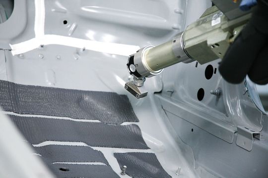 Mit moderner Technik können Dämmungsmassen automatisiert, das heißt per Roboter, in den Fußraum eines Autos eingebracht werden. Diese "spritzbare Akustikmasse" (SAM) wird im sogenannten Flatstream-Verfahren aufgetragen. Mit moderner Technik können Dämmungsmassen automatisiert, das heißt per Roboter, in den Fußraum eines Autos eingebracht werden. Diese "spritzbare Akustikmasse" (SAM) wird im sogenannten Flatstream-Verfahren aufgetragen.